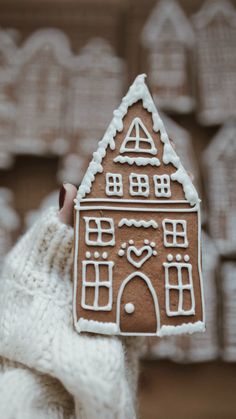 someone holding up a gingerbread house shaped cookie