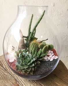 a glass vase filled with succulents and rocks on top of a wooden table