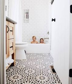 two people are sitting in the bathtub with black and white tiles on the floor