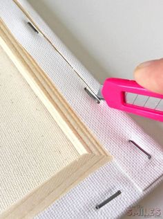 a person holding a pink pair of scissors near a piece of wood with holes in it