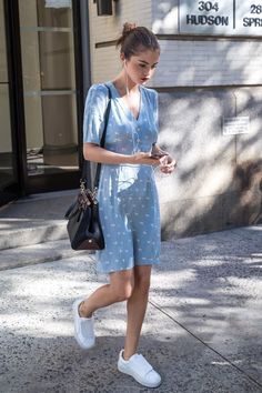 a woman is walking down the street while looking at her cell phone and wearing white sneakers