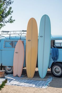 three surfboards are lined up in front of a blue vw camper van