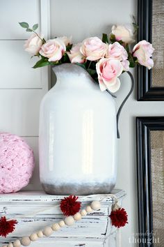 a white vase filled with pink flowers on top of a table