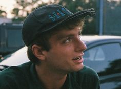 a young man wearing a hat and looking off to the side in front of parked cars