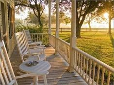 two white rocking chairs sitting on a porch next to a tree and grass covered field