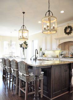 a large kitchen with an island in the middle and chairs at the end, along with two chandeliers hanging from the ceiling