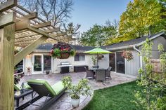 an outdoor patio with chairs, table and grill in the back yard is surrounded by greenery