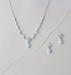 a white necklace and earring set on a gray surface with flowers in the background