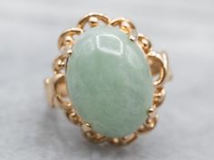 This stunning Mid Century mounting is a rich combination of yellow gold and soft mint green jade. The metalwork around the stone ripples with petal-like scalloping, with just a wonderful polish framing this lovely stone. This would make a great and different cocktail ring, and the color is truly superb!Metal: 14K Yellow GoldGem: JadeGem Measurements: 16.0 x 11.9 mm, OvalRing Size: 4.50Marks: “14K” Stamped on the inside band Ring Green Stone, Soft Mint Green, Green Stone Ring, Soft Mint, Green Stone Rings, White Gold Sapphire, Black Hills Gold, Oval Ring, Cabochon Ring