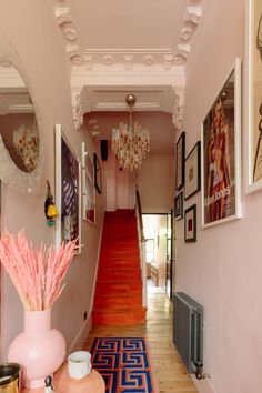 the hallway is decorated in pink and blue with pictures on the wall, chandelier, and rug