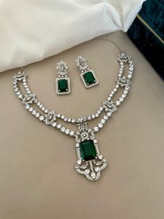 A luxurious Emerald Green and Diamond necklace set in a double layer string for the gorgeous woman, lusciously crafted with American diamonds and emerald stones. An exquisite Designer Set perfect for any occasion.  Details: Necklace Width at Centre-2.5 Inches Earrings Length-1.5 Inches Weight of Each Earring-5.7 gms All products are manufactured using traditional skills from our rich heritage of crafts.  The process of these crafts is essentially manual. Hence, any irregularities or variations a Luxury Traditional American Diamond Necklace, Formal Bridal Necklace With 17 Jewels And Emerald, Elegant Formal Bridal Necklace With Emerald, Elegant Emerald Bridal Necklace For Formal Occasions, Elegant Formal Emerald Bridal Necklace, Elegant Emerald Bridal Necklace, Elegant Emerald Bridal Necklace For Wedding, Elegant Emerald Necklace With Elegant Design, Wedding Emerald Necklace In Fine Jewelry Style