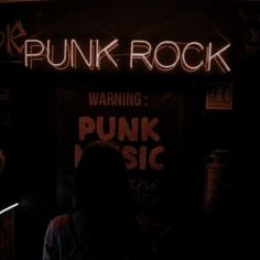 a person standing in front of a punk rock sign with neon writing on the wall