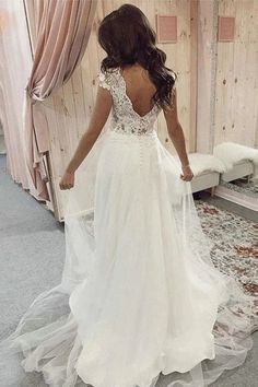 a woman in a white wedding dress looking at herself in the mirror with her back to the camera