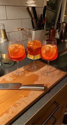 three glasses of wine sitting on top of a wooden cutting board next to a knife