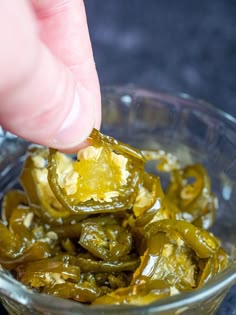 someone is picking up some green peppers in a glass bowl