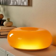 an orange light sitting on top of a counter next to books and vases in a room