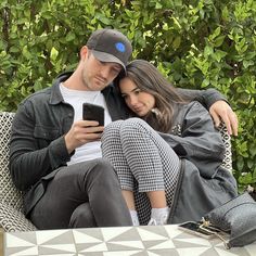 a man and woman are sitting on a bench looking at their cell phones while they look at the screen