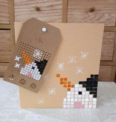 a cross stitch card with a penguin and snowflakes on it, next to a wooden drawer