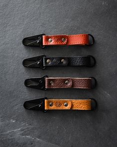 three leather key fobs are lined up on a gray surface with black handles