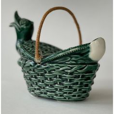 a small green basket with a bird on the handle and a white egg in it