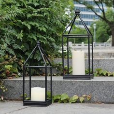 two black lanterns with white candles sitting on some steps