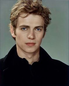 a young man with curly hair and blue eyes looks at the camera while wearing a black shirt