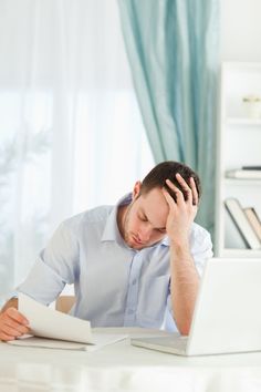 a man sitting at a desk with his head in his hands while looking at a laptop