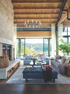 a living room filled with furniture and a fire place under a chandelier in front of a large window