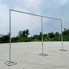 three metal poles are standing in the middle of a concrete area with trees in the background