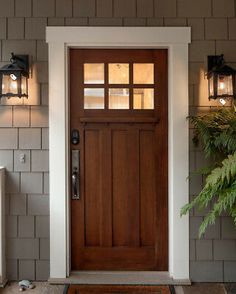 a front door with two lights on the side and a plant next to it outside