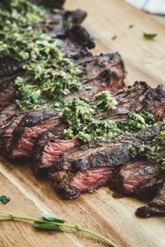 steak with pesto on it sitting on a cutting board next to some green herbs