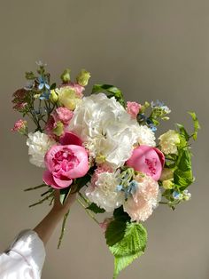 a woman holding a bouquet of white and pink flowers with green leaves in her hand