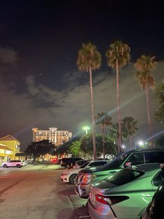 cars parked in a parking lot at night with palm trees and buildings in the background