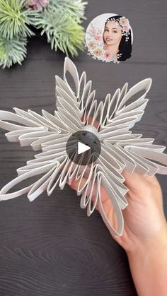 a person holding an origami flower on top of a table next to succulents