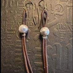 pair of brown leather earrings with silver beads on them, hanging from hooks in front of an egyptian background