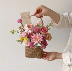 a woman holding a basket with flowers in it and a thank you card attached to the handle