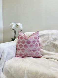 a pink pillow sitting on top of a bed next to a vase with white flowers