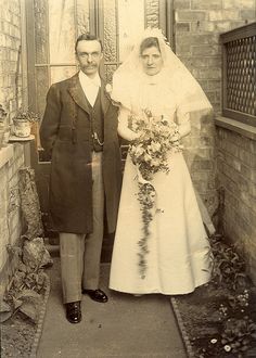 an old black and white photo of a man and woman in wedding attire standing outside