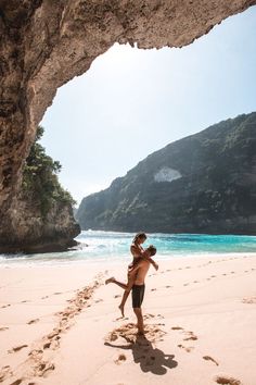 two people are playing on the beach under an arch