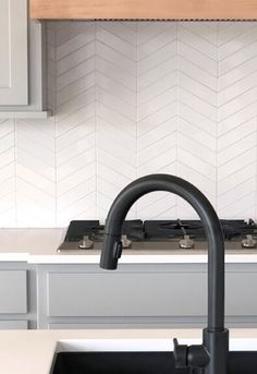 a kitchen sink with a black faucet in the middle and white tiles on the backsplash