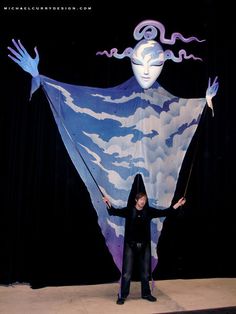 a woman standing on top of a stage with her hands in the air while holding onto a giant kite