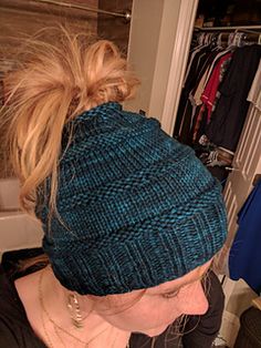 a woman with blonde hair wearing a blue knitted beanie in front of a closet