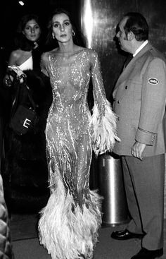 an old photo of a woman in a feathered dress and man standing next to her