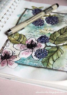 a close up of a notebook with flowers and leaves on it next to a pen