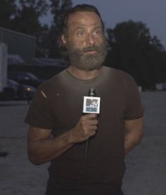 a man with a beard holding a microphone in front of his face and looking at the camera