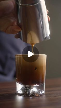 someone pouring coffee into a glass on top of a wooden table