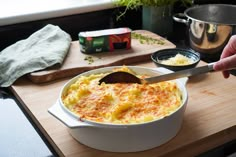 a person is spooning food out of a casserole dish on a cutting board