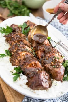 someone is spooning sauce over some meat on top of rice and garnished with parsley