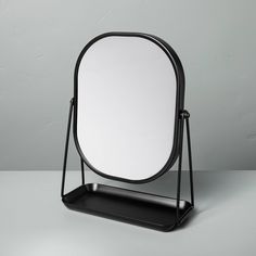 a round mirror sitting on top of a black stand next to a white wall and floor