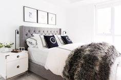 a bed with white sheets and black pillows in a bedroom next to a dresser, framed pictures on the wall